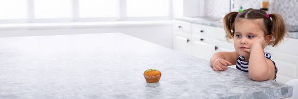 Close-up Of Girl Looking At Cupcake On Kitchen Worktop - Foto, Imagem