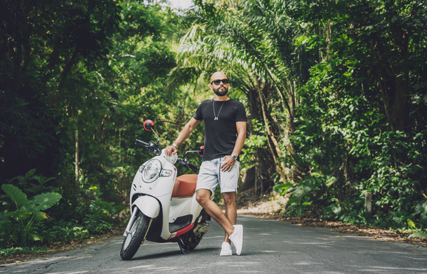 Stylish young man and his motorbike on the road in the jungle - Photo, image
