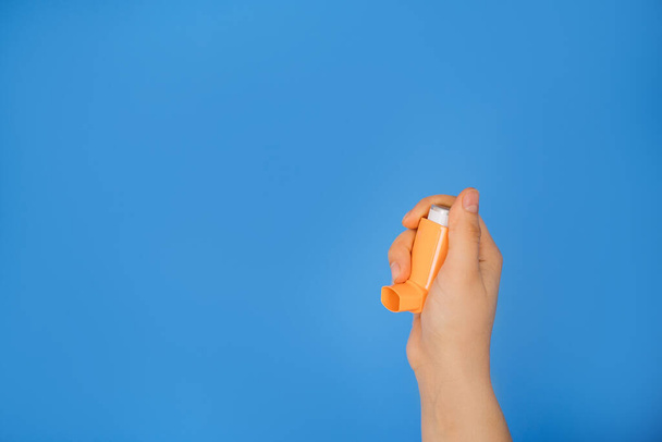 A hand holds an asthma inhaler on a blue background. World Asthma Day. The concept of allergy treatment. Copy space - Fotografie, Obrázek