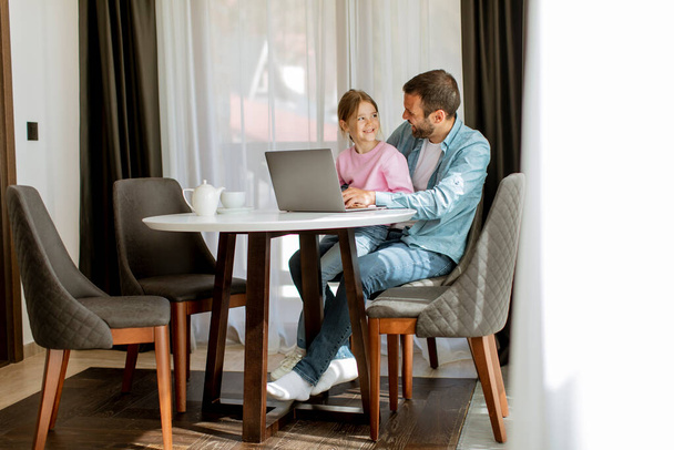 Отец и дочь используют ноутбук вместе в комнате - Фото, изображение