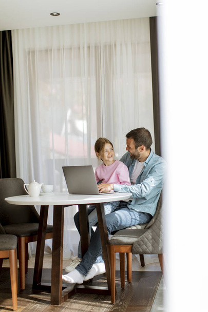 Батько і дочка використовують ноутбук разом у кімнаті
 - Фото, зображення