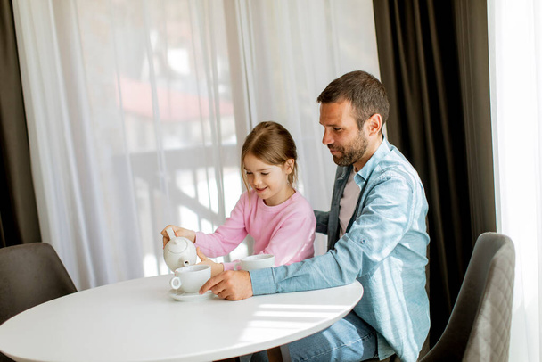 Батько і дочка п'ють чай разом у вітальні
 - Фото, зображення