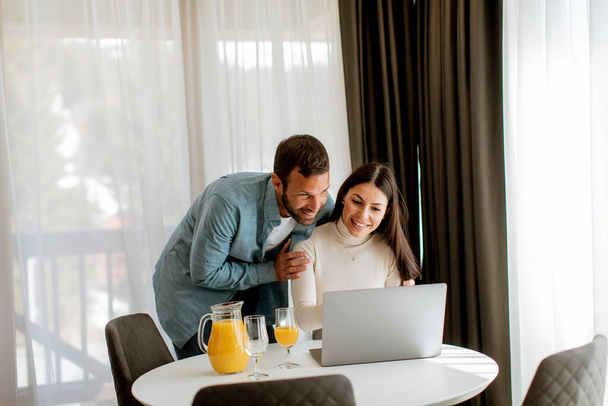 Молода пара використовує ноутбук на столі у вітальні і п'є апельсиновий сік
 - Фото, зображення