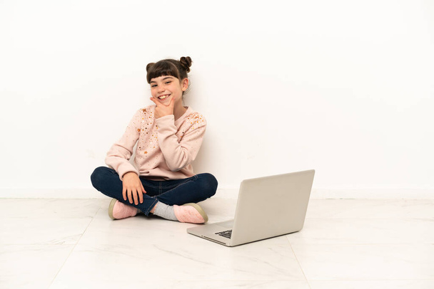 Egy kislány laptoppal a padlón ül boldogan és mosolyogva. - Fotó, kép
