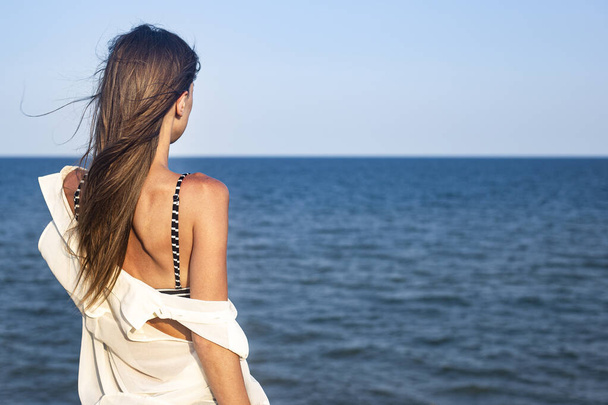Piękna seksowna młoda kobieta w jasnym pareo na klifie patrzy na morze  - Zdjęcie, obraz