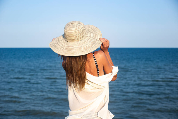 Junge Frau mit Hut auf einer Klippe blickt an einem Sommertag aufs Meer  - Foto, Bild