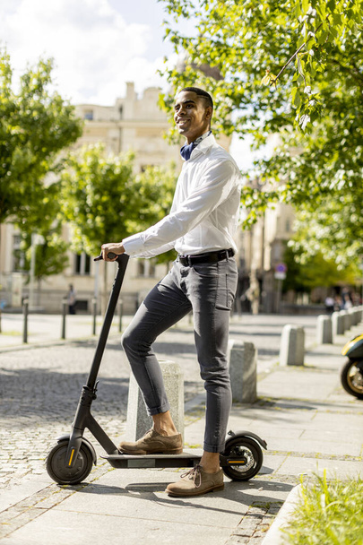 Beau jeune Afro-Américain utilisant scooter électrique sur une rue - Photo, image