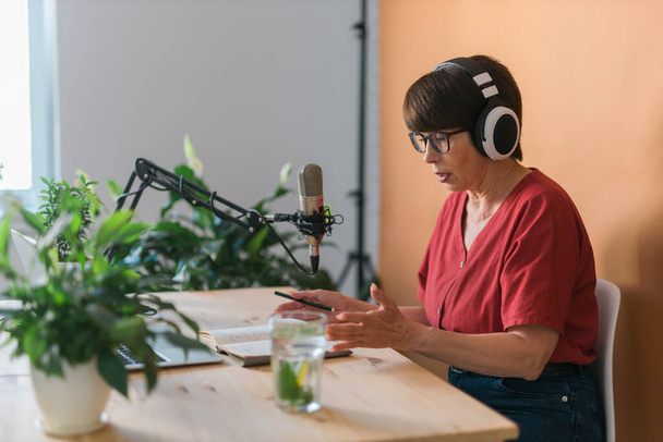 Middle-aged female radio presenter talking into the microphone and reading news - radio broadcast online concept - Photo, Image