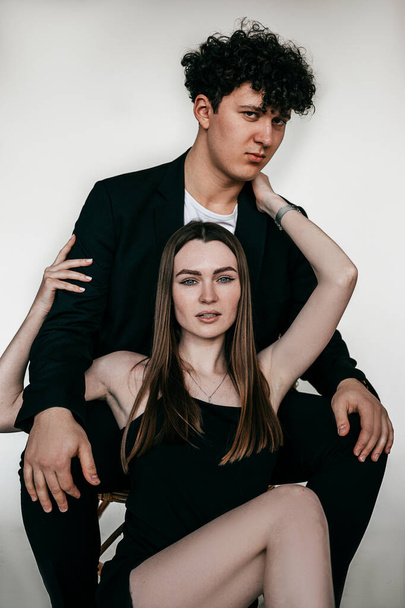 Hot couple embracing posing and wearing elegant black outfits and accessories for men and women, white background. Glamour fashion style catalog of clothes for business people, trends of formal wear - Фото, изображение