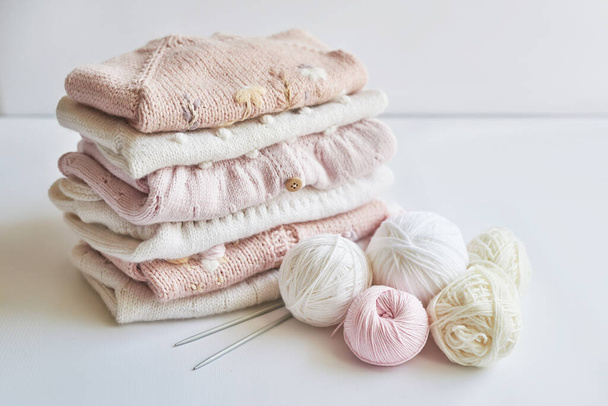 Stack of knitted clothes and balls of yarn, knitting needles, accessories for knitting. Baby clothes. Needlework, hobby, knitting, handwork - Φωτογραφία, εικόνα