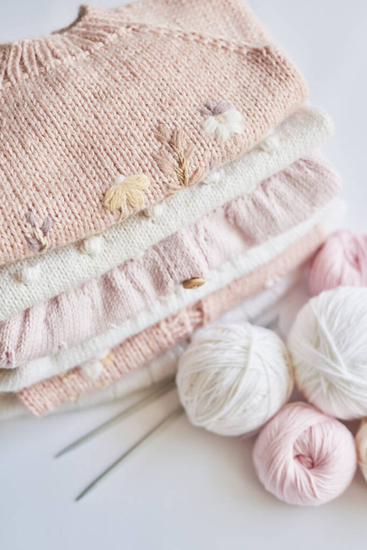 Stack of knitted clothes and balls of yarn, knitting needles, accessories for knitting. Baby clothes. Needlework, hobby, knitting, handwork - Photo, Image