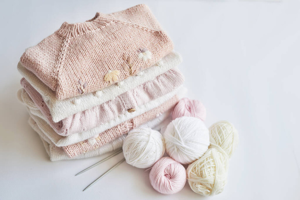 Stack of knitted clothes and balls of yarn, knitting needles, accessories for knitting. Baby clothes. Needlework, hobby, knitting, handwork - Fotografie, Obrázek