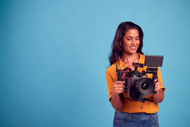 Mature Female Videographer With Camera Filming Video Against Blue Background On Shoot In Studio - Foto, Imagen