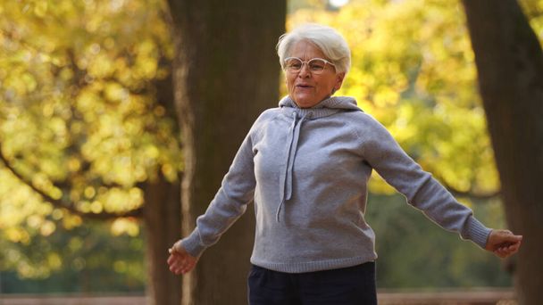Fitness concept. Being physically active in the old age pays off. Outdoor shot of caucasian pensioner lady in gray hoodie jogging. - Fotografie, Obrázek