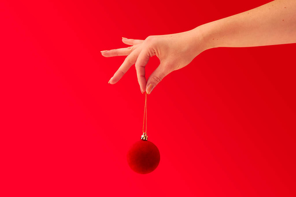 Close Up Studio Shot Of Woman Holding Christmas Tree Decoration Against Red Background - Фото, зображення