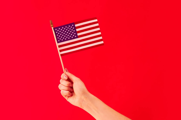 Close Up Studio Shot Of Female Hand Holding Stars And Stripes American Flag Against Red Background - Foto, afbeelding