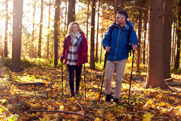 Front View Of Mature Retired Couple Walking Through Fall Or Winter Countryside Using Hiking Poles - Photo, image