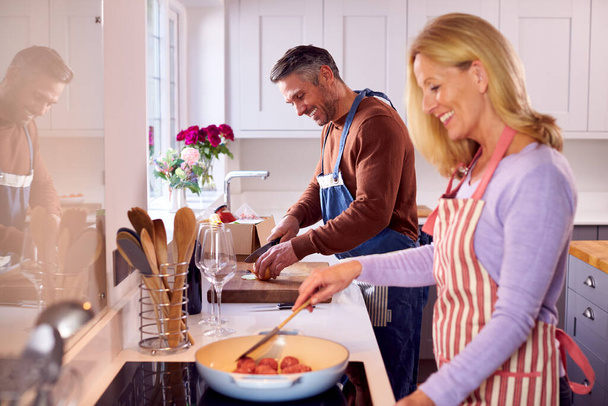Mature Couple At Home In Kitchen Chopping Ingredients And Cooking In Pan Prepare Meal Together - 写真・画像
