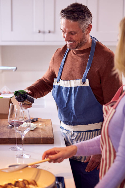 Mature Couple At Home In Kitchen Drinking Red Wine As They Prepare Meal Together - Valokuva, kuva
