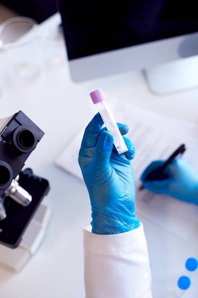 Close Up Of Lab Worker Conducting Research Using Microscope Holding Tube With PCR Test Swab - Foto, Imagen