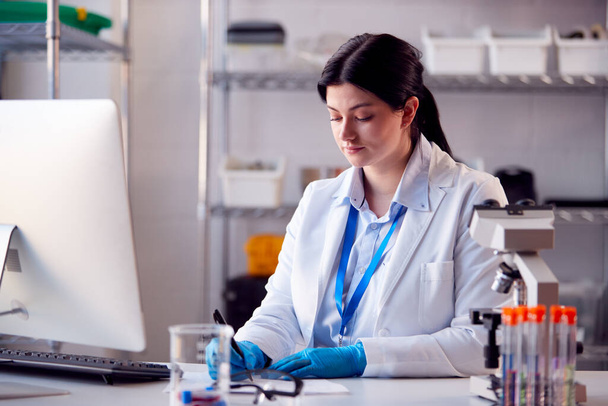 Female Lab Worker Wearing White Coat Recording Test Results On Computer - Foto, imagen