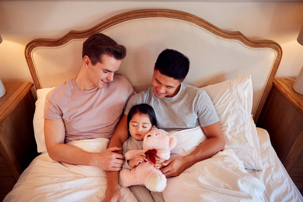 Evde yatağında kızıyla ve yumuşak oyuncağıyla oyun oynayan iki babayla aile fotoğrafı. - Fotoğraf, Görsel