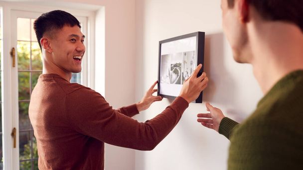 Same Sex Male Couple Hanging Picture On Wall At Home Together - Foto, afbeelding