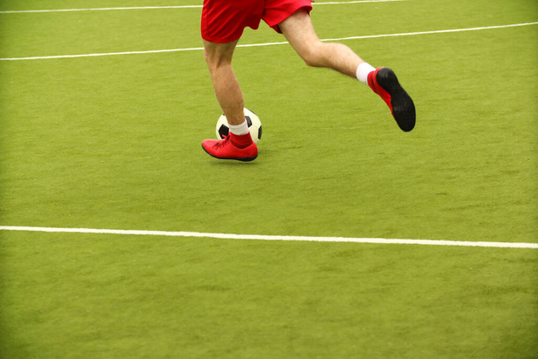 Οι παίκτες παίζουν μίνι ποδόσφαιρο στο γήπεδο. Πόδια, αθλητικά και μια μπάλα. Πράσινο γήπεδο ποδοσφαίρου. - Φωτογραφία, εικόνα