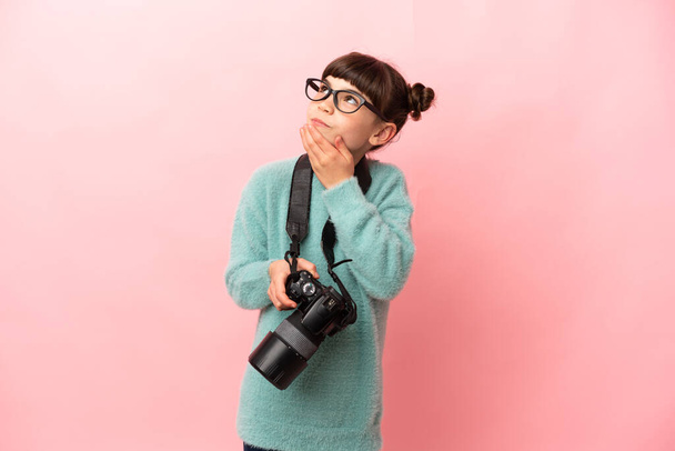 Little photographer girl isolated on pink background looking up while smiling - Fotografie, Obrázek