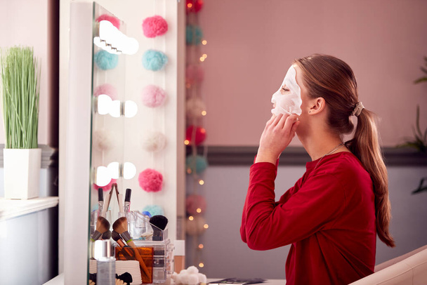 Teenage Girl Wearing Pyjamas Putting On Face Mask In Bedroom At Home - Fotoğraf, Görsel