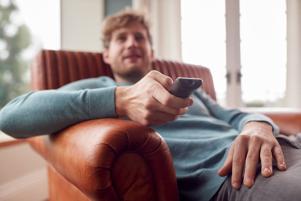 Man Sitting Relaxing On Armchair At Home Watching TV Using Remote Control - Valokuva, kuva