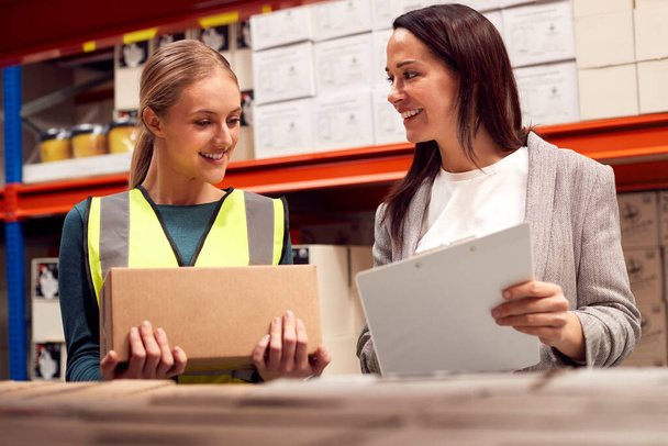 Female Team Leader With Clipboard In Warehouse Training Intern Standing By Shelves - Фото, изображение