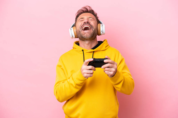 Uomo di mezza età che gioca con un controller di videogiochi isolato su sfondo rosa ridendo - Foto, immagini