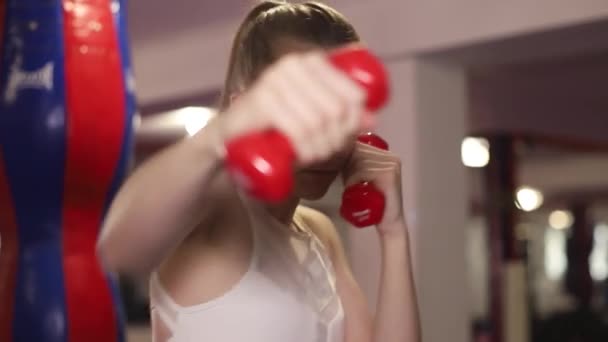 Lány bokszoló gyakorlatok ütések súlyzókkal a kezében. Edzés a boxteremben.  - Felvétel, videó