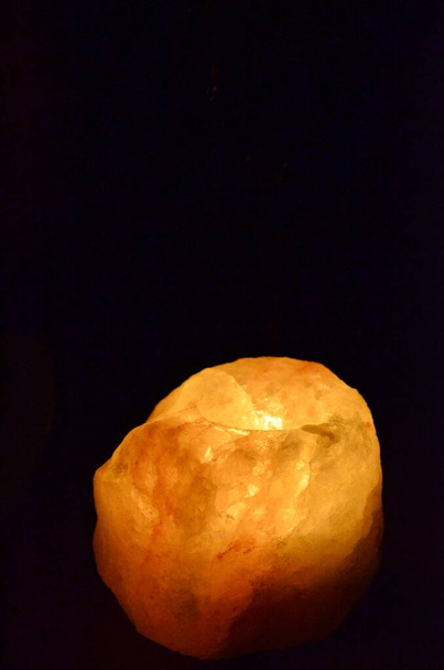 Μια λάμπα αλατιού λάμπει στο σκοτάδι. Φυσικό πορτοκαλί φως φωτιάς. - Φωτογραφία, εικόνα