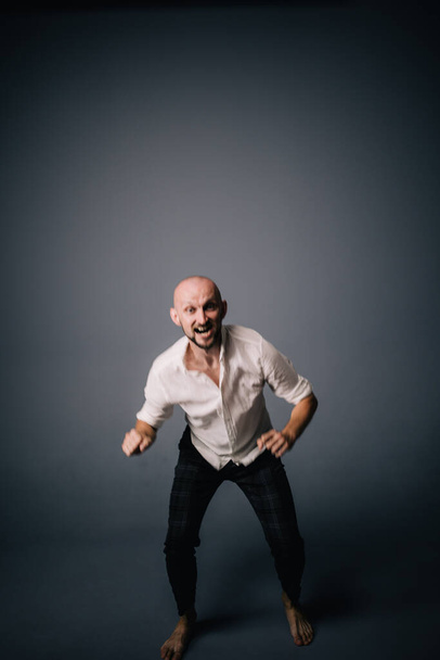 studio portrait of a bald guy with a beautiful beard barefoot in a white shirt and plaid pants dancing on a gray background - Φωτογραφία, εικόνα