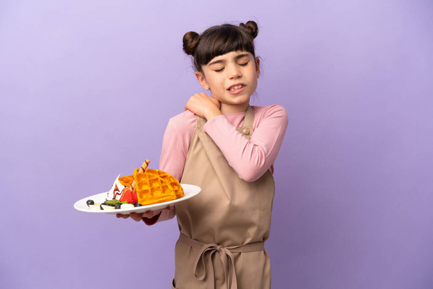 Klein blank meisje houden wafels geïsoleerd op paarse achtergrond die lijden aan pijn in de schouder voor het hebben van een inspanning - Foto, afbeelding