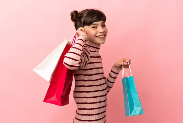 Pequeña chica caucásica aislada sobre fondo rosa sosteniendo bolsas de compras y sonriendo - Foto, imagen