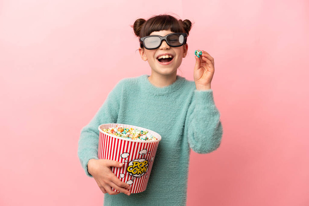 mały kaukaski dziewczyna izolowane na różowy tło z 3d okulary i trzymając duży wiadro popcorns - Zdjęcie, obraz