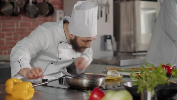 Mannelijke chef-kok gieten versnipperde kaas op gekookt voedsel in koekenpan - Video