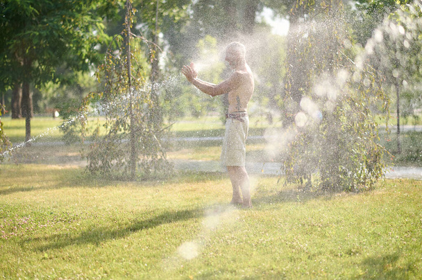 A half-naked man in shorts standing under shower in the park - Valokuva, kuva