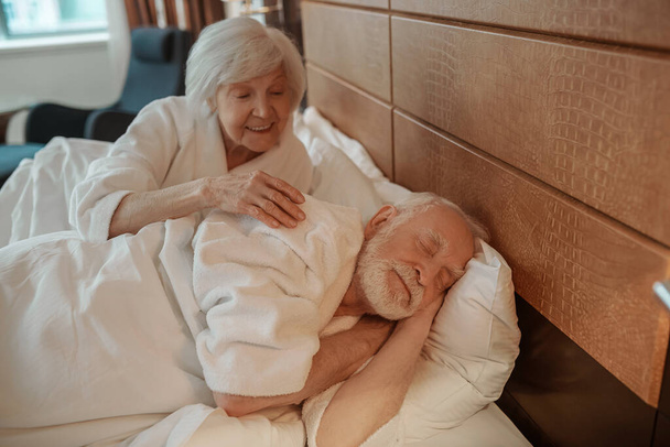 A senior couple in bed in the morning in a hotel room - Zdjęcie, obraz