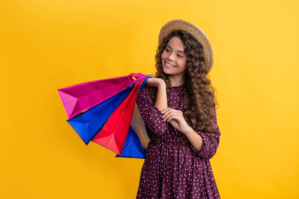 smile child with curly hair hold shopping bags on yellow background - Fotografie, Obrázek