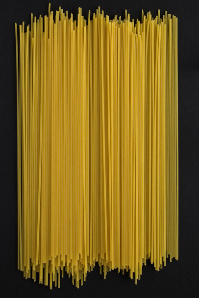 Close-up on italian spaghetti on the black background. Top view. Location vertical. - Фото, изображение