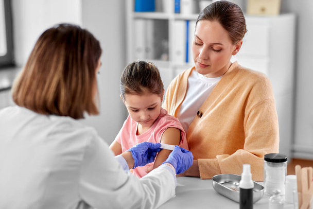doctor sticking patch to childs arm at clinic - Foto, Imagen