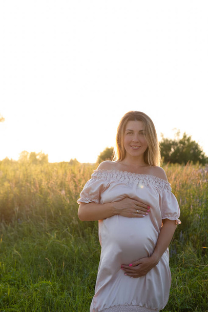 Zwangerschaps portret bij zonsondergang. Verwachtte dat moeder buiten zou zijn in roze jurk. Mooie tedere stemmingsfoto van zwangerschap - Foto, afbeelding