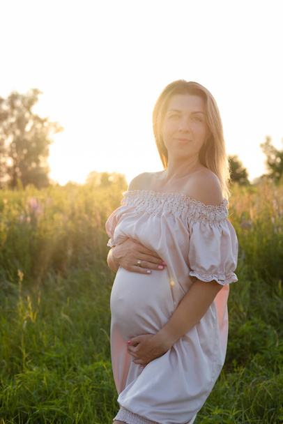 Zartes Schwangerschaftsporträt im Sonnenuntergang. Die werdende Mutter wird draußen in rosa Kleid sein. Schöne zarte Stimmung Foto der Schwangerschaft - Foto, Bild
