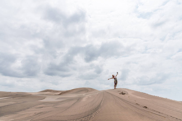 Photo with copy space of a woman gesturing freedom in the middle of a desert in a cloudy day - Fotó, kép