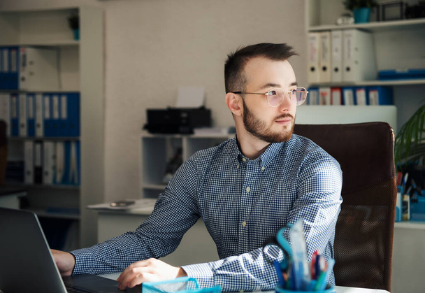 Νεαρός επιχειρηματίας με πουκάμισο που δουλεύει στο λάπτοπ του σε ένα γραφείο - Φωτογραφία, εικόνα