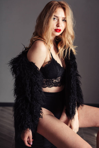 A girl with red lips in a top sits in a fur coat with a side - Foto, Imagen